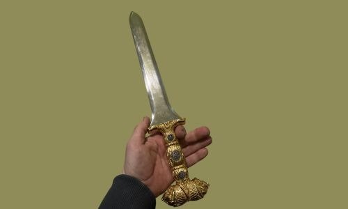 A person holding a large Akinakes sword with a gold-trimmed blade, showcasing its ornate design and craftsmanship.