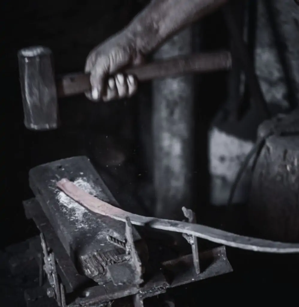 a bladesmith forging persian sword using hammer on tempered steel